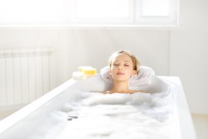 An Attractive girl relaxing in bath on light background
